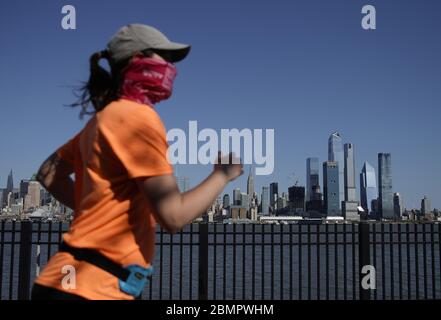 Hoboken, Vereinigte Staaten Von Amerika. Mai 2020. Eine Frau trägt eine schützende Gesichtsmaske, während sie am Sonntag, den 10. Mai 2020 in Hoboken, New Jersey, joggt und dabei das Empire State Building, die Hudson Yards und die Skyline von Manhattan betrachtet. Die Coronavirus-Pandemie hat in New York City 20,000 Menschen getötet und weltweit über 270 00 Todesfälle. Foto von John Angelillo/UPI Quelle: UPI/Alamy Live News Stockfoto