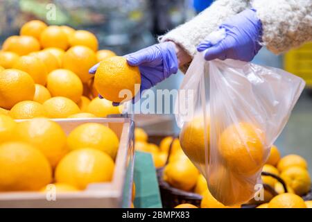 Frau Hände in medizinischen Handschuhen wählt frische Orangen Falten in einem Einweg-Plastiktüte im Supermarkt, Nahaufnahme. Schutzmaßnahmen gegen Coronavi Stockfoto