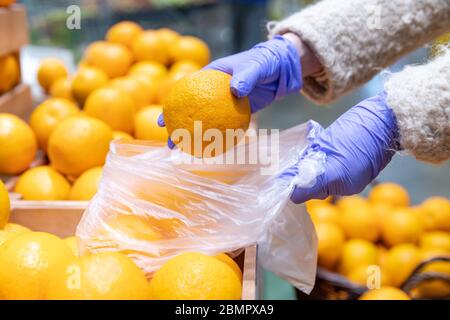 Frau Hände in medizinischen Handschuhen wählt frische Orangen Falten in einem Einweg-Plastiktüte im Supermarkt, Nahaufnahme. Schutzmaßnahmen gegen Coronavi Stockfoto