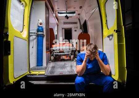 Verwirrt Sanitäter in einer blauen Uniform sitzen im Rücken Eines Ambulanzwagens Stockfoto