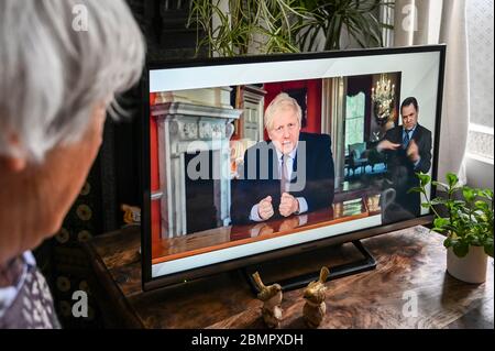 Boris Johnson mit einer Fernsehrede aus Downing Street während der Covid-Pandemie, die Änderungen der Sperrpolitik behandelt, die von einem Zuschauer beobachtet werden. Stockfoto