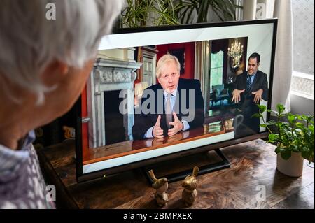 Boris Johnson mit einer Fernsehrede aus Downing Street während der Covid-Pandemie, die Änderungen der Sperrpolitik behandelt, die von einem Zuschauer beobachtet werden. Stockfoto