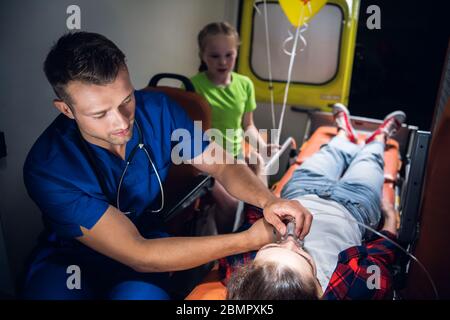 Ein Sanitäter legt eine Sauerstoffmaske auf ein Unbewusstes Frau liegt auf einer Bahre im Ambulanzwagen Stockfoto