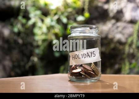 Ein Glas mit Münzen innen und ein 'vacaciones'-Anhänger auf einem Holz. UN bote de Cristal con monedas dentro, tiene una etiqueta que pone vacaciones sobre Stockfoto