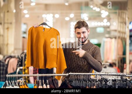 Ein junger Mann wählt Kleidung für seine Freundin in einem Kaufen Stockfoto