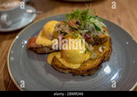 Eier benedikt auf Sauerteig Toast mit Grüns und Hollandaise Sauce. Pochierte Eier im rustikalen Stil auf einem grauen Teller Stockfoto