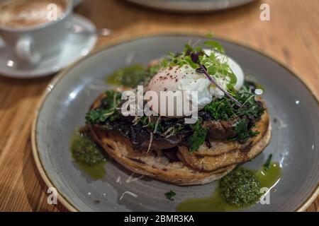 Eier benedikt auf Sauerteig Toast mit Grüns, Pesto und Pilzen. Pochierte Eier im rustikalen Stil auf einem grauen Teller Stockfoto