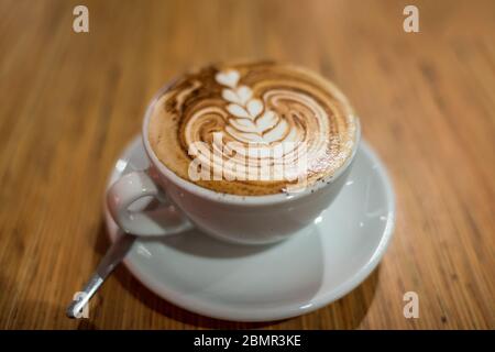 Kaffee trinken in einer weißen Tasse. Flacher weißer Kaffee oder Cappuccino mit Schaukelkunst in der Tasse im Café Stockfoto
