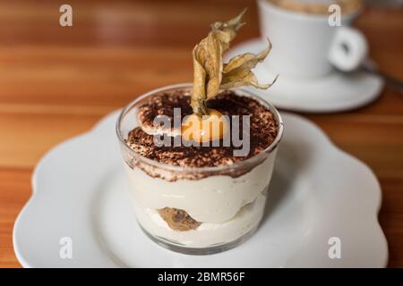 Tiramisu Dessert in einem Glas mit Physalis-Beere und Kaffeetasse auf dem Hintergrund dekoriert Stockfoto