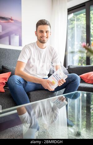 Haan, Deutschland. Mai 2020. Tim Nießner sitzt mit seinem Buch "die geheimen Tricks der 1.0 Schüler" auf einer Couch. Der 18-Jährige aus Haan bei Düsseldorf hat sich etwas Besonderes einfallen lassen, um sich auf sein Abitur vorzubereiten: Er hat fast 100 der besten Abiturienten Deutschlands interviewt, um herauszufinden, was er von ihnen lernen kann. Daraus entstand ein 300-seitiges Buch mit dem Titel: "Die geheimen Tricks der 1,0er-Schüler" 1.0, das am 12.05.2020 im mvg Verlag erscheinen wird. Bild: Marcel Kusch/dpa/Alamy Live News Stockfoto