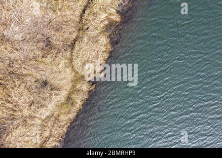 Trockenes Gras am Flussufer und Wasser mit Himmelsreflexion. Natürliche Muster. Luftdrohne Ansicht Stockfoto