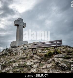 Alte verwitterte Stein kalvarienberg in der Nähe einer Holzbank auf einem felsigen Berg versiegelt Stockfoto