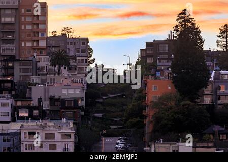 Die berühmte krumme Lombard Street in San Francisco, Kalifornien, mit einer kultigen Seilbahn auf dem Hügel und einem feurigen Himmel bei Sonnenuntergang Stockfoto