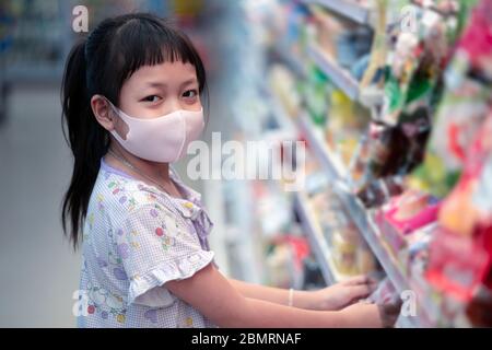 Einkaufskonzept mit asiatischen Kindern während des Virus-Ausbruchs. Kind trägt chirurgische Gesichtsmaske Kauf Obst im Supermarkt in Coronavirus Pandemie. Kleines b Stockfoto