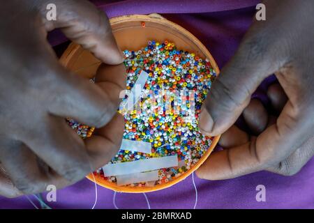 Herstellung von handgefertigtem Schmuck. Box mit Perlen und afrikanischen Frauenhände, Draufsicht, Nahaufnahme. Insel Sansibar, Tansania, Ostafrika Stockfoto