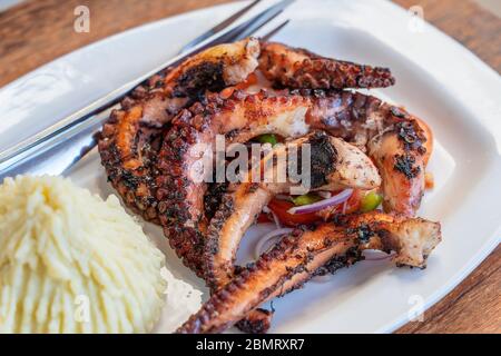 Gebratene Kraken Tentakeln mit Kartoffelpüree und Gemüsesalat auf einem weißen Teller, Nahaufnahme Stockfoto