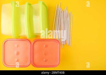 Kunststoff-Lunchboxen und Trinkhalme auf gelbem Hintergrund, bunte Kunststoff-Container Stockfoto