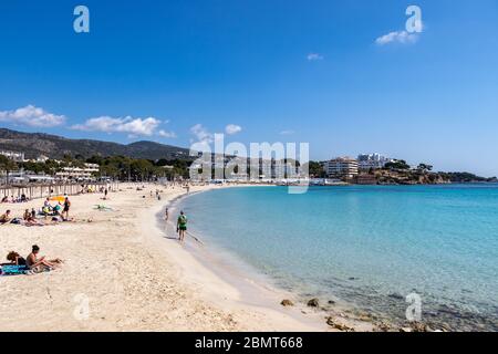 Palmanova, Mallorca, Spanien - 13. April 2019: Touristen, die ein Sonnenbad am Strand Platja de Palmanova, Mittelmeer, Balearen. Stockfoto