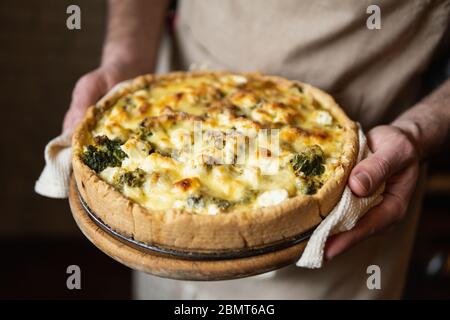 Männliche Hände halten Käse und Broccoli Quiche Tart. Hausmannskost nach französischem Rezept. Stockfoto