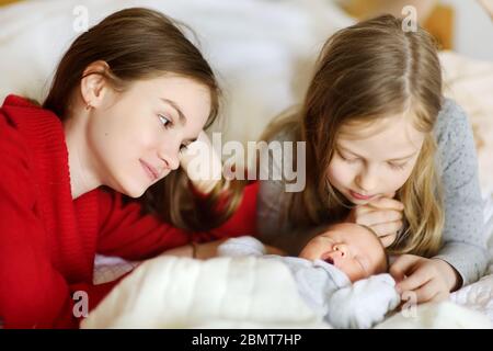 Zwei große Schwestern bewundern ihren schlafenden neugeborenen Bruder. Zwei junge Mädchen halten ihren neuen Jungen. Kinder mit großem Altersunterschied. Ein großer Altersunterschied zwischen den beiden Stockfoto