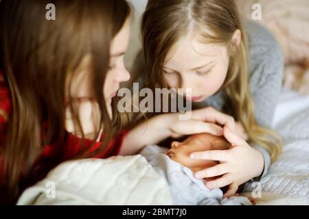 Zwei große Schwestern bewundern ihren schlafenden neugeborenen Bruder. Zwei junge Mädchen halten ihren neuen Jungen. Kinder mit großem Altersunterschied. Ein großer Altersunterschied zwischen den beiden Stockfoto