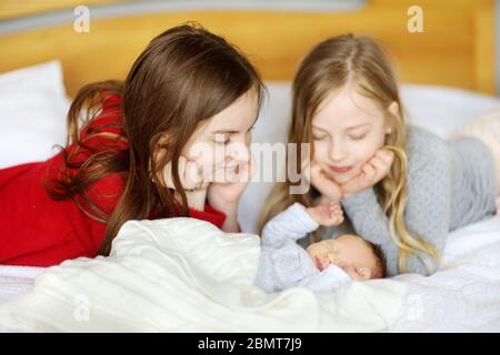 Zwei große Schwestern bewundern ihren schlafenden neugeborenen Bruder. Zwei junge Mädchen halten ihren neuen Jungen. Kinder mit großem Altersunterschied. Ein großer Altersunterschied zwischen den beiden Stockfoto