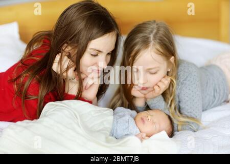 Zwei große Schwestern bewundern ihren schlafenden neugeborenen Bruder. Zwei junge Mädchen halten ihren neuen Jungen. Kinder mit großem Altersunterschied. Ein großer Altersunterschied zwischen den beiden Stockfoto