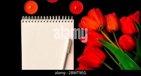 Rote Tulpen, leere Karte oder Notizblock mit Stift und Kerzen auf schwarzem Hintergrund isoliert, kopieren Raum für Text Stockfoto