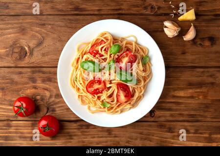 Spaghetti in Tomatensauce mit Käse und Basilikum auf Holzhintergrund. Blick von oben Stockfoto