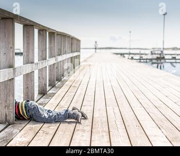 Ein Kind, das auf dem Bauch auf einem Pier liegt und auf das Wasser schaut. Stockfoto