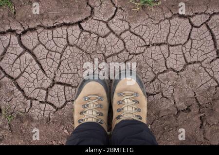 Beine in Wanderschuhen auf dem rissigen, getrockneten Boden Stockfoto