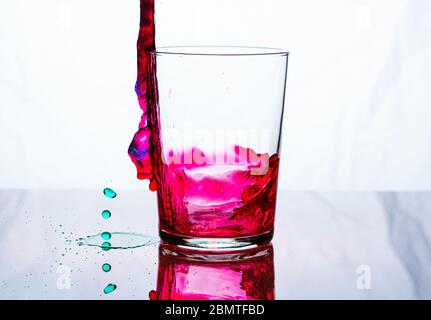 Ein Glas, das mit rosa und grüner Flüssigkeit gefüllt wird. Weißer Hintergrund.. Stockfoto