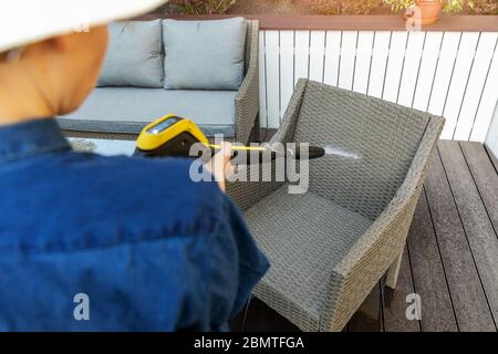Frau tut Gartenterrasse Möbel Reinigung mit Hochdruckreiniger Stockfoto
