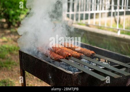 Traditionelles türkisches Adana Kebap auf dem Grill mit Spiessen zum Abendessen. Türkische Küche Esskultur in der Türkei. Adana Kebab auf dem mangal in der Natur Stockfoto