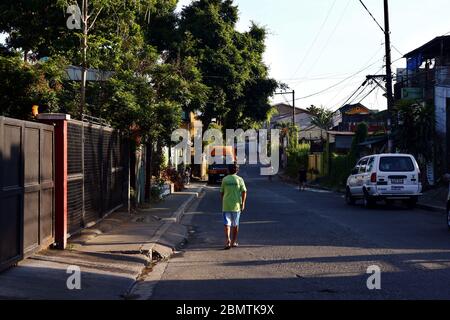 Antipolo City, Philippinen - 11. Mai 2020: Mann, der bei Sonnenaufgang eine leere Straße entlang geht und einen schönen Sonnenstrahl hat. Stockfoto