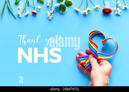 Danke NHS, Ärzte, Krankenschwestern, medizinische Teams und Schlüsselarbeiter in England und Großbritannien! Hand hält Regenbogen Band in Herzform auf blauem Minze Hintergrund wi Stockfoto