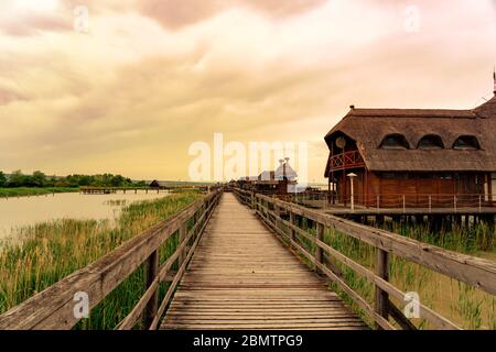 Ruhige Natur am Fertő See in Ungarn mit Holzsteg Bungalows Hütten am See und Stroh im Wasser bei Sonnenuntergang Stockfoto