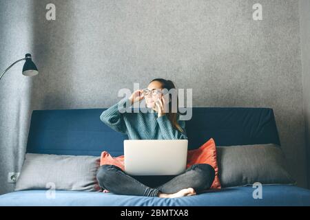 Ein Mädchen arbeitet von zu Hause oder ein Student studiert von zu Hause oder als Freiberufler. Sie verwendet einen Laptop und ein Telefon. Stockfoto