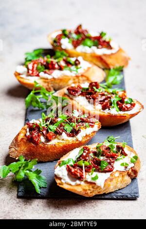 Toasts mit sonnengetrockneten Tomaten und Frischkäse auf schwarzem Brett, dunkler Hintergrund. Stockfoto