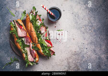 Zwei frische Baguette-Sandwiches mit Fleisch, Tomaten, Gurken und Rucola auf grauem Hintergrund. Stockfoto