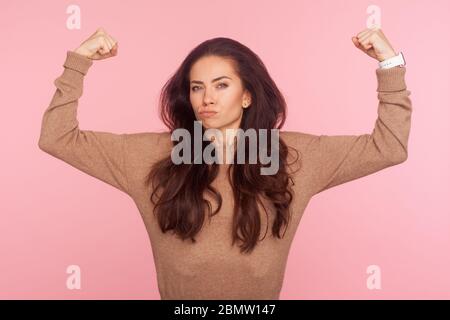 Konzept der weiblichen Macht und Unabhängigkeit. Selbstbewusste tapfere junge Frau mit brünetten Haaren in Pullover Heben Hände Bizeps zeigen, zum Ausdruck Stärke Stockfoto