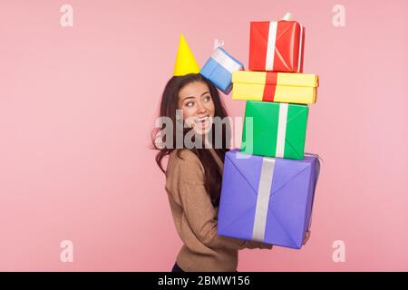 Porträt der freudigen überrascht junge Frau mit Party-Kegel und mit Staunen auf viele Geschenkboxen in ihren Händen, genießen viele der besten Geschenke, Stockfoto