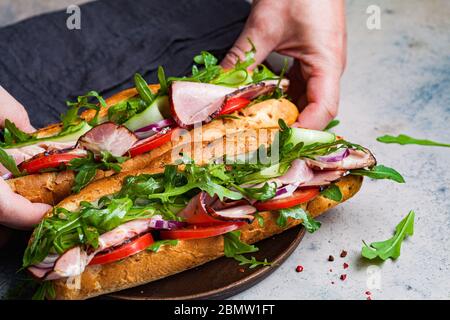 Zwei frische Baguette-Sandwiches mit Fleisch, Tomaten, Gurken und Rucola auf grauem Hintergrund. Stockfoto