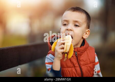 Kleiner Junge essen Banane in der Natur.Glückliches Kind genießen Sie das Essen von frischem Obst. Gesundes Essen, Menschen und Lifestyle-Konzept. Stockfoto