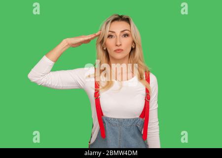 Ja, Herr! Portrait der verantwortungsbewussten disziplinierten erwachsenen Frau in stilvollen Denim Overalls salutieren und hören, um zu bestellen wirh ernst aufmerksamen Ausdruck. Stockfoto