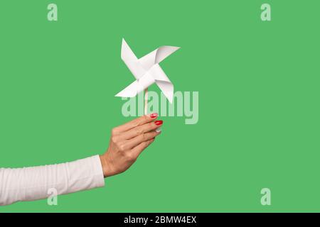 Nahaufnahme des weiblichen Arm hält Pinwheel Spielzeug auf Stick, Origami Handmühle isoliert auf grünem Hintergrund, zeigt Papier Windmühle, weißen Spinner Chi spielen Stockfoto