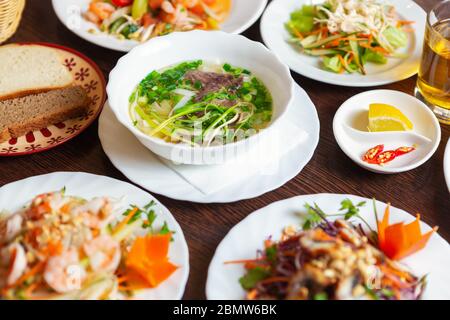 Asiatische Küche auf dem Tisch im Restaurant.köstliche Pho bo Suppe und Meeresfrüchte Salate in weißen Platten serviert.leckere exotische vietnamesische Küche mit natürlichen Ingred Stockfoto