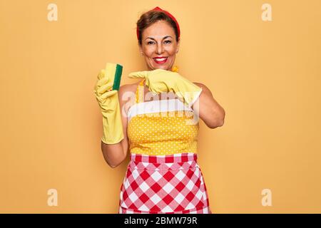 Mittelalter Senior Hausfrau Pin-up Frau trägt 50s Stil Retro-Kleid mit Reiniger Peeling sehr glücklich zeigen mit Hand und Finger Stockfoto