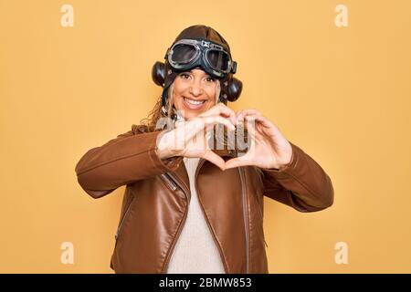 Junge schöne blonde Fliegerfrau trägt vintage Pilot Helm, dessen Brille und Jacke lächelnd in Liebe tun Herz Symbol Form mit Händen. Romanti Stockfoto