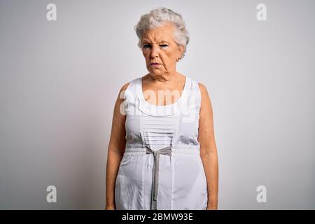 Senior schöne grauhaarige Frau, die lässig Sommerkleid über weißem Hintergrund skeptisch und nervös, Stirnrunzeln aufgeregt wegen des Problems. Negativ Stockfoto